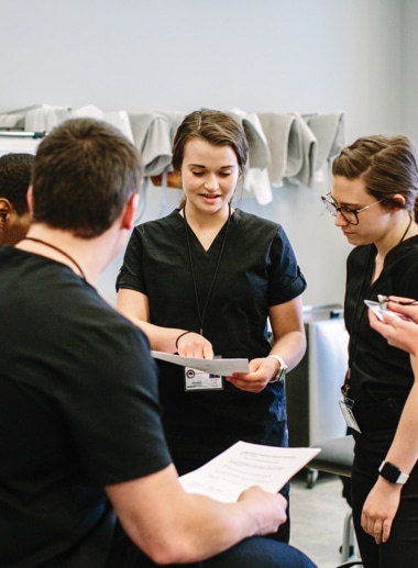 A group of healthcare students, dressed in black scrubs, are having a discussion.